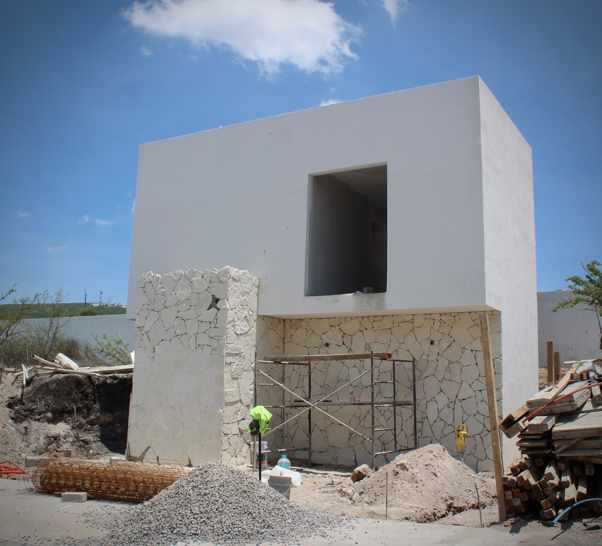 Fachada en construcción — volumen superior, muro de piedra y vanos principales.